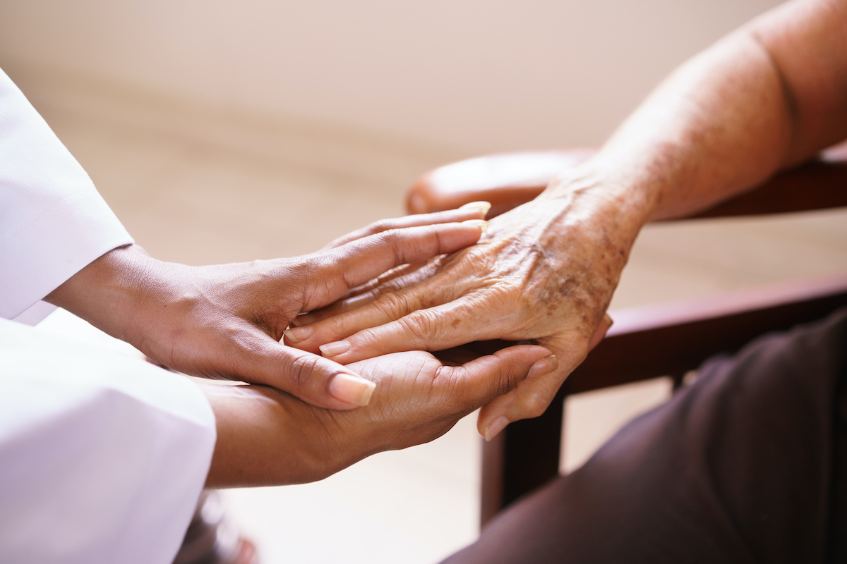 Old people in geriatric hospice: Aged patient receives the visit of a female black doctor. They shake their hands and talk in the hospital.