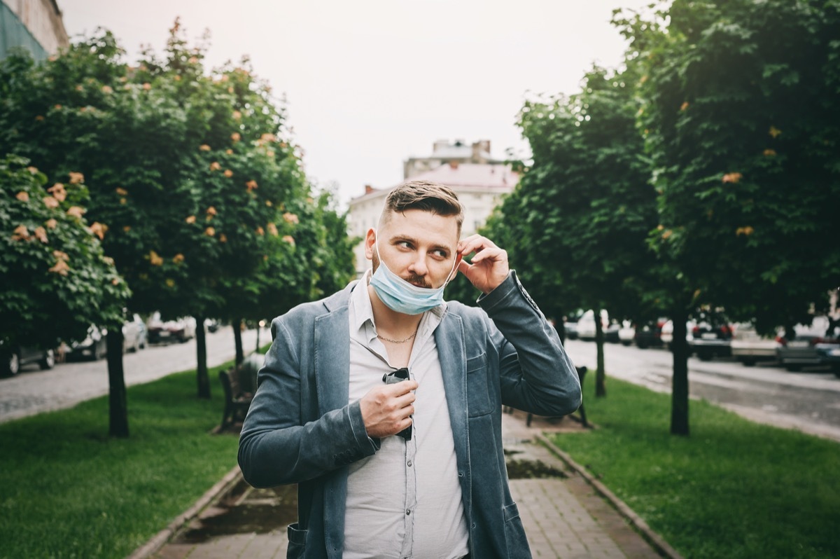 middle aged white man wearing surgical mask under chin while walking outdoors