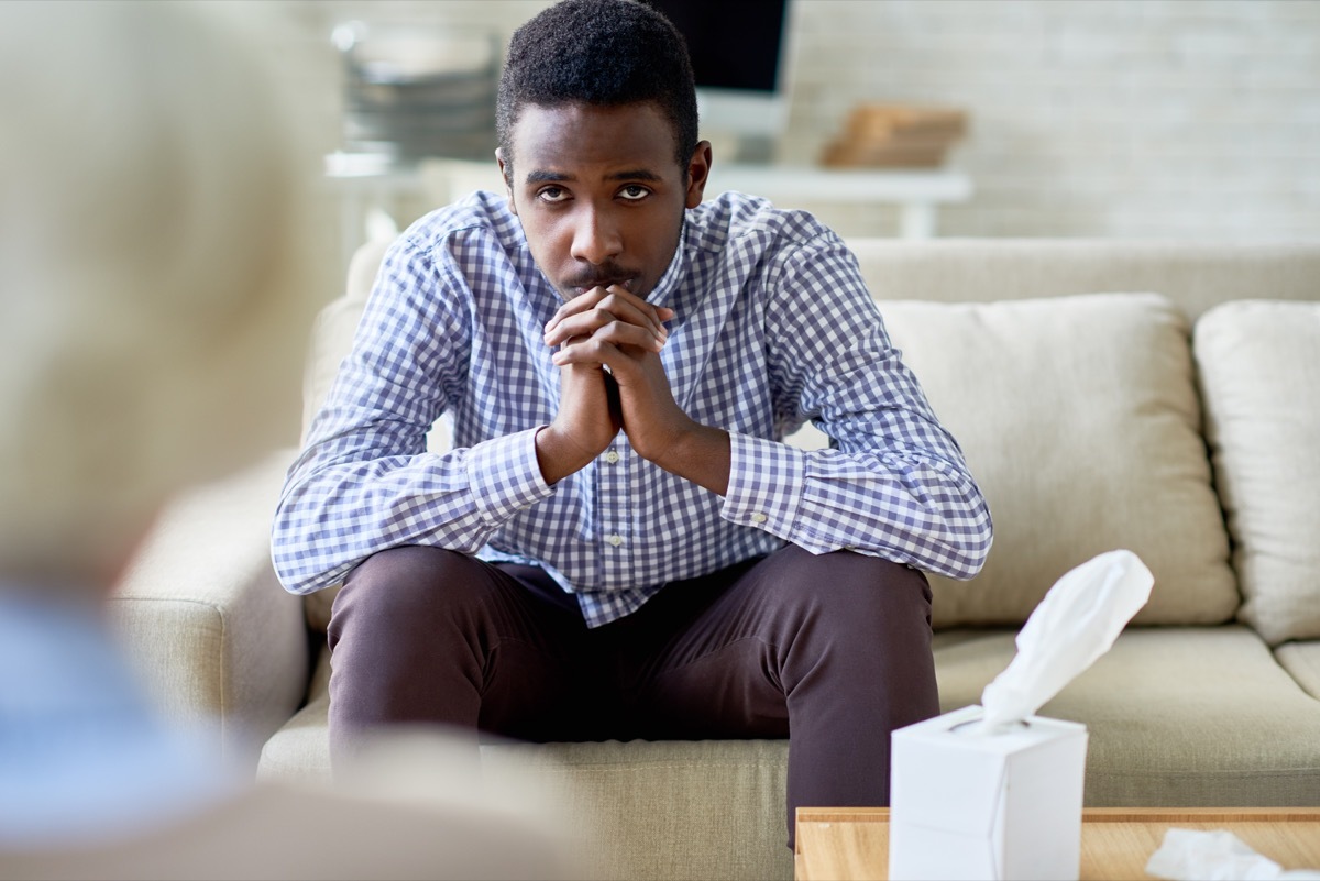 Depressed man sitting on sofa in psychotherapy office and listening to advice