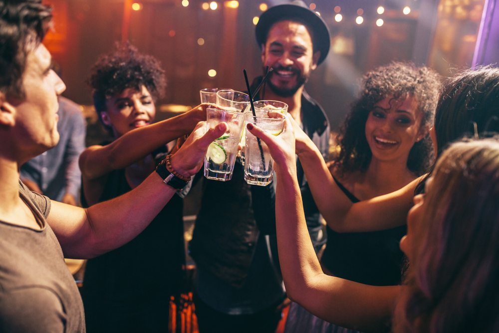 Friends toasting at bar on a night out drinking alcohol