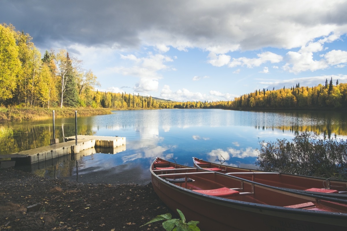 Pier and two red canoes on the Talkeetna lakes, open lake, autumn trees and reflection of clouds.