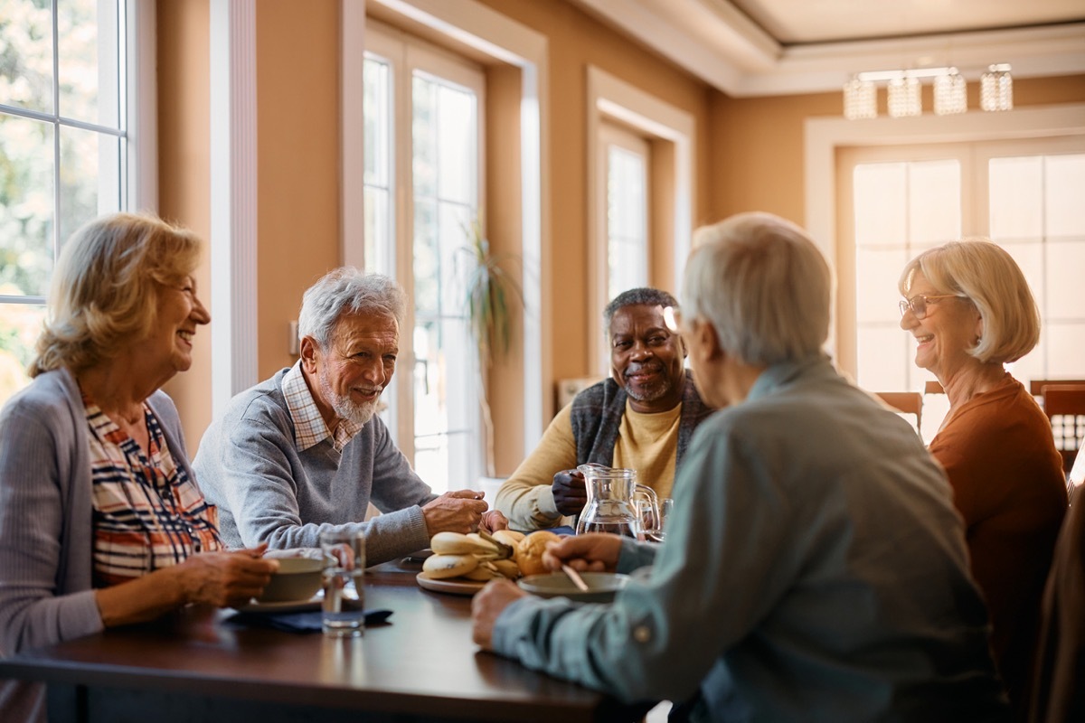 Group of senior people enjoying in conversation during lunch at dining table at nursing home.