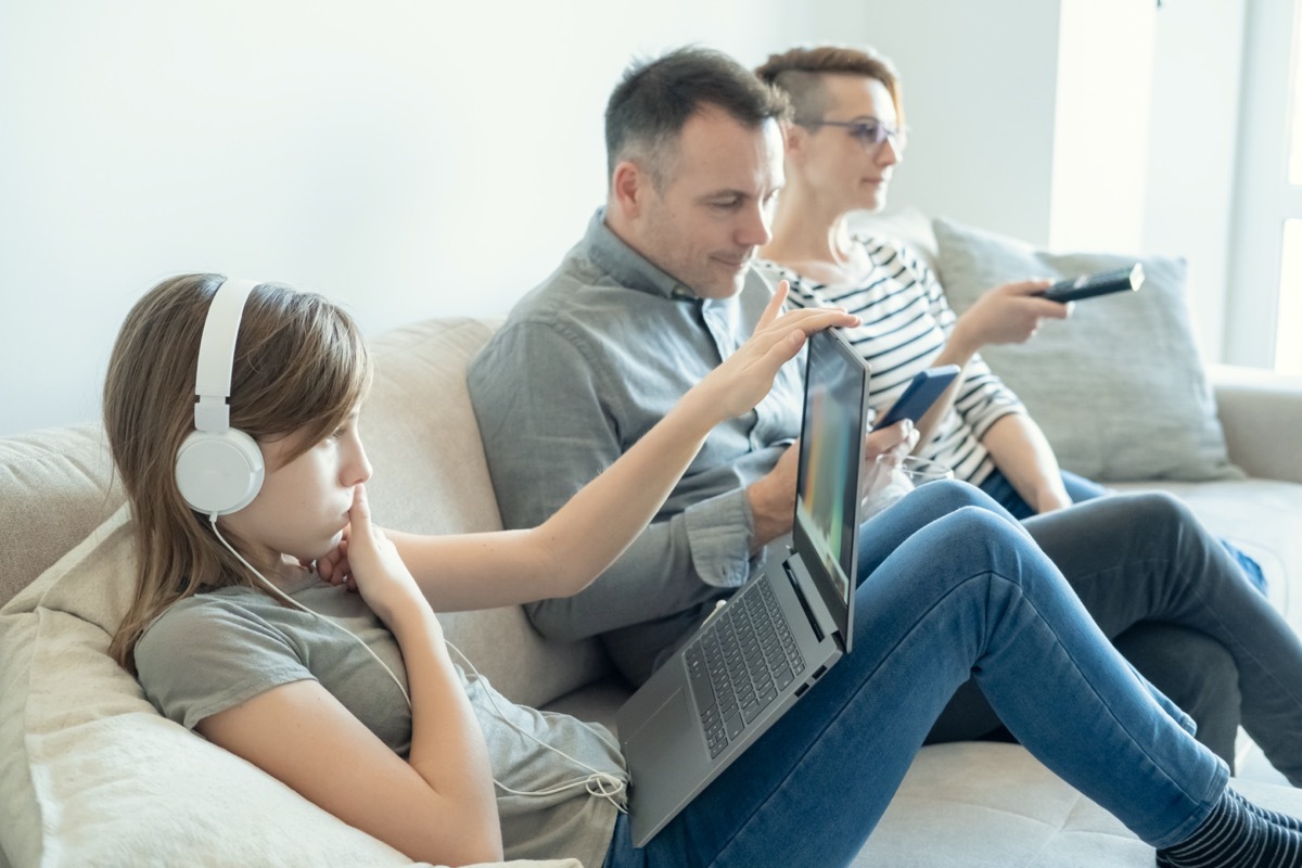 young girl using laptop on bed while mom and dad watching TV and not paying attention to her