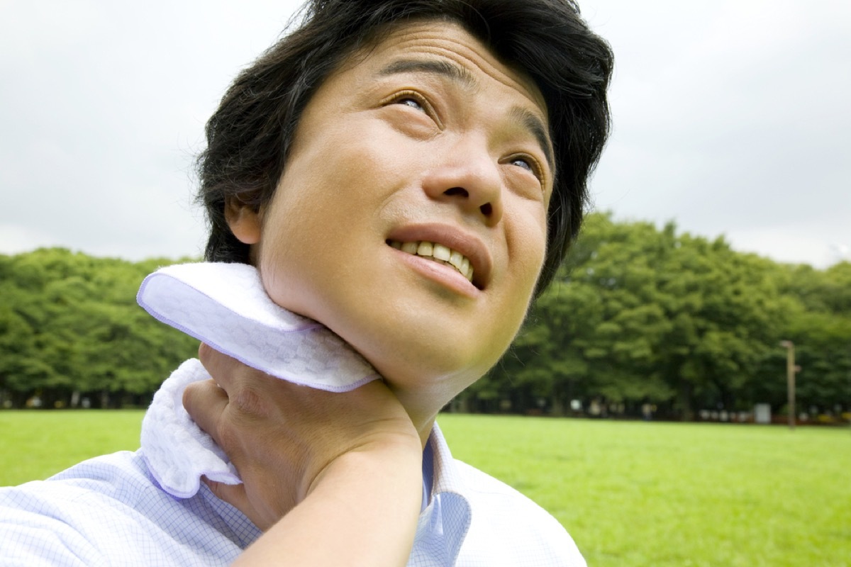 asian man wiping neck and looking up at the sun outside