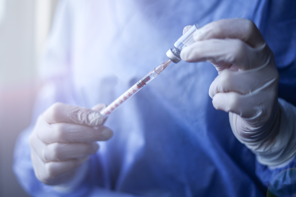 A healthcare worker wearing gloves fills a syringe with COVID-19 vaccine