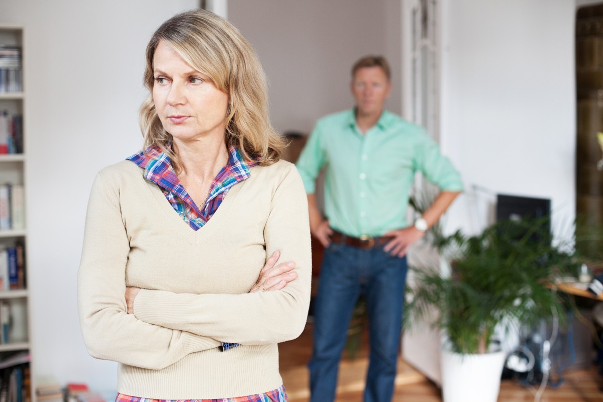 middle aged white woman with arms crossed and husband in background