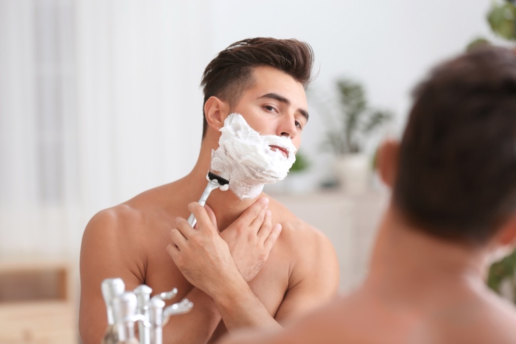 man shaving off shaving cream in front of a mirror