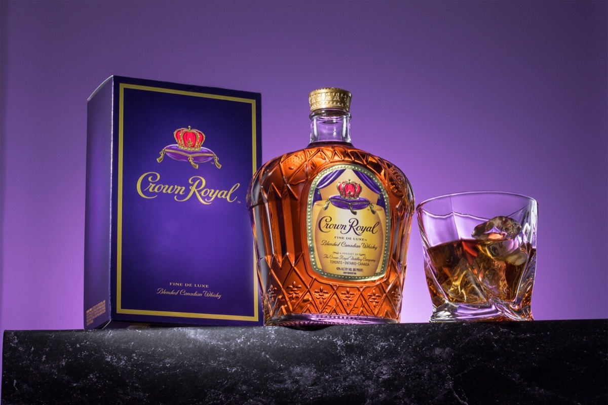 Bottle of Crown Royal, a glass, and a box in front of a purple background