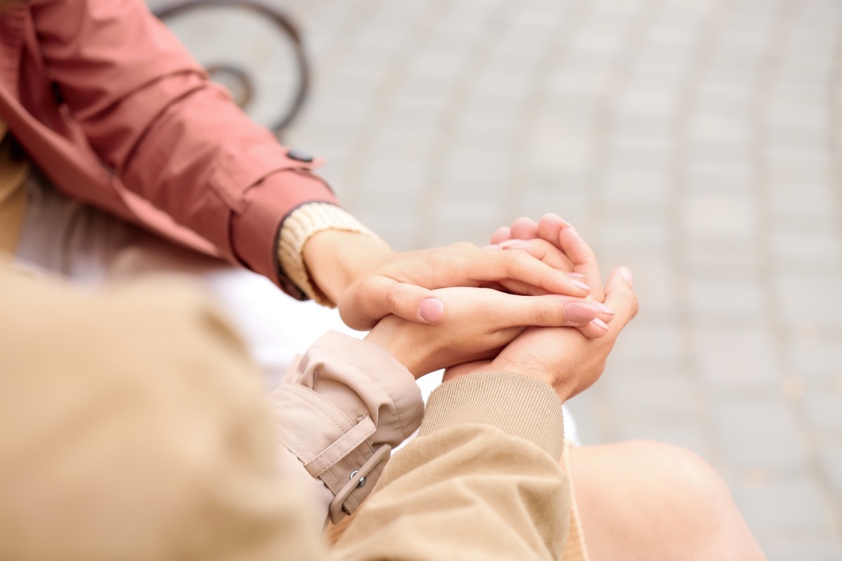 Man with two beautiful women holding hands outdoors. Polyamory concept