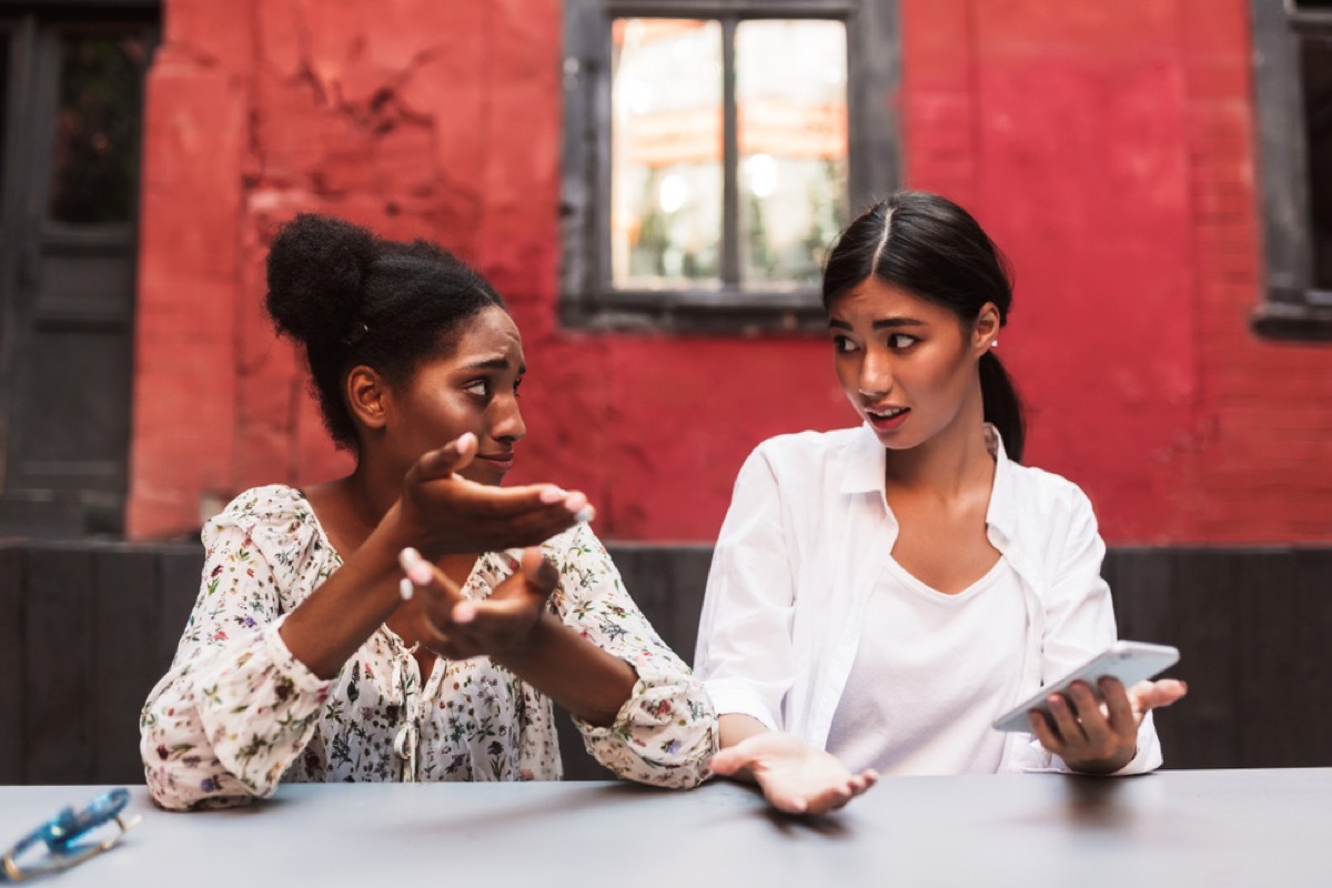 young black and asian women arguing outdoors in front of red building