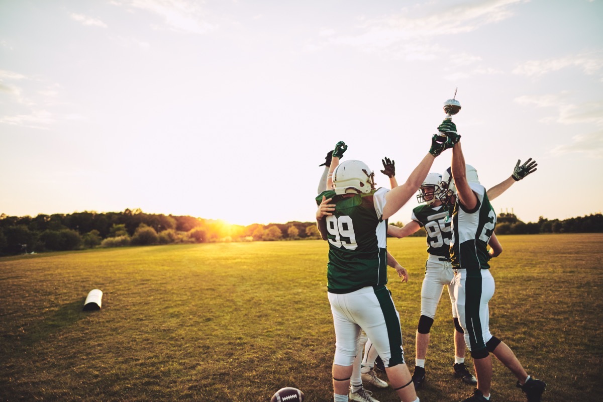 Football players standing together in a huddle and raising a championship trophy