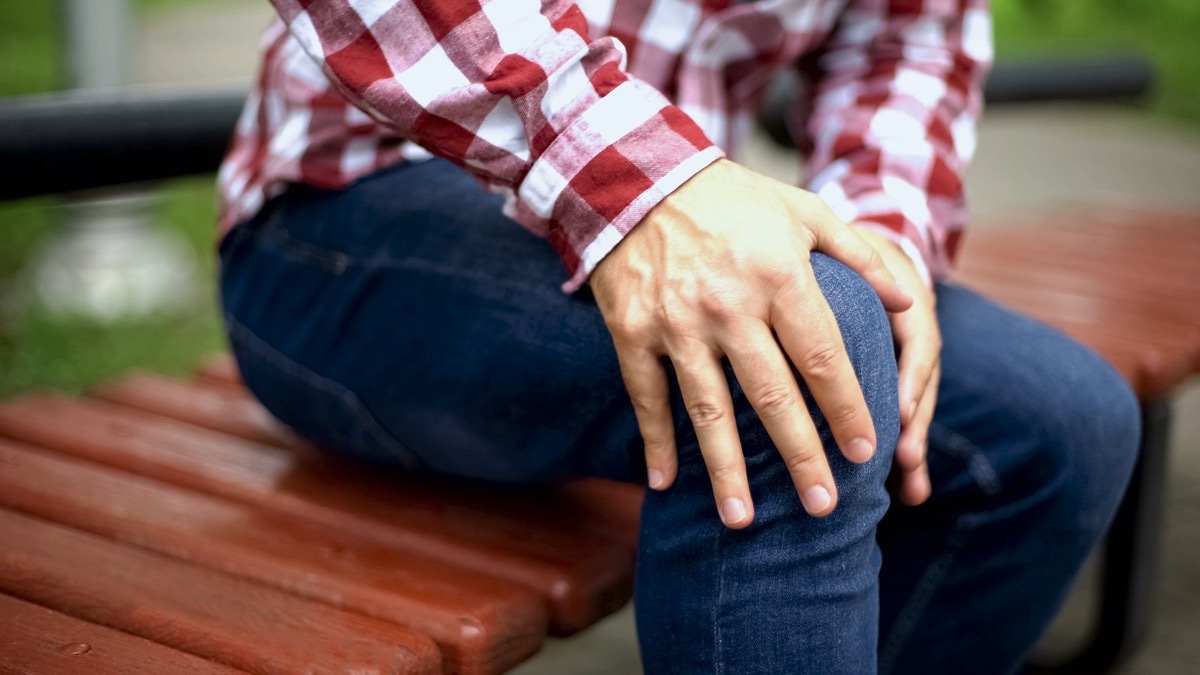 Man massaging painful knee, suffering from pain, injury