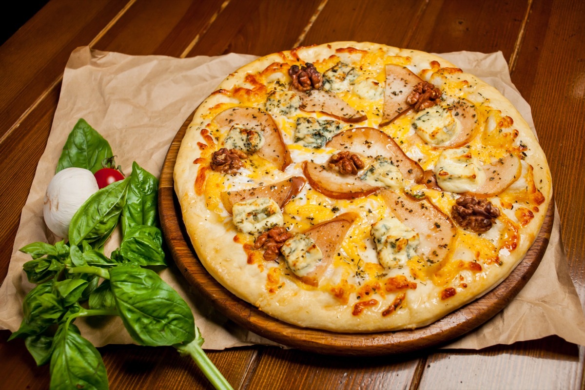 Pear and Gorgonzola Pizza sitting on a a wood table surrounded by fresh basil