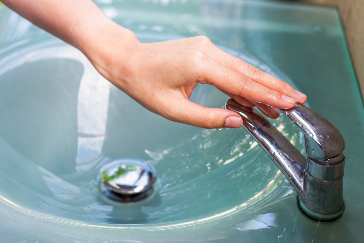 A close up of a person turning off a faucet.