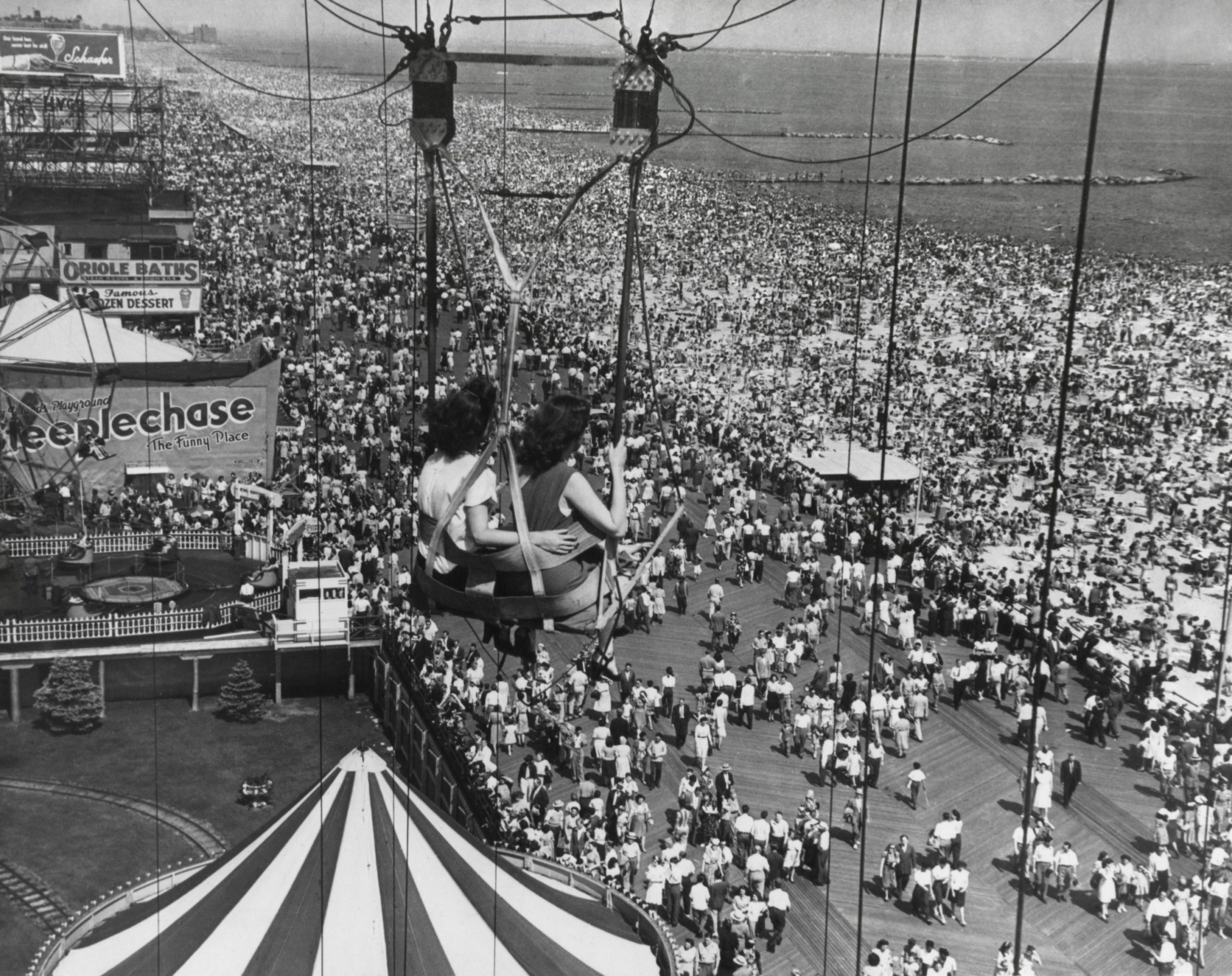 two young women sit on swings overlooking coney island