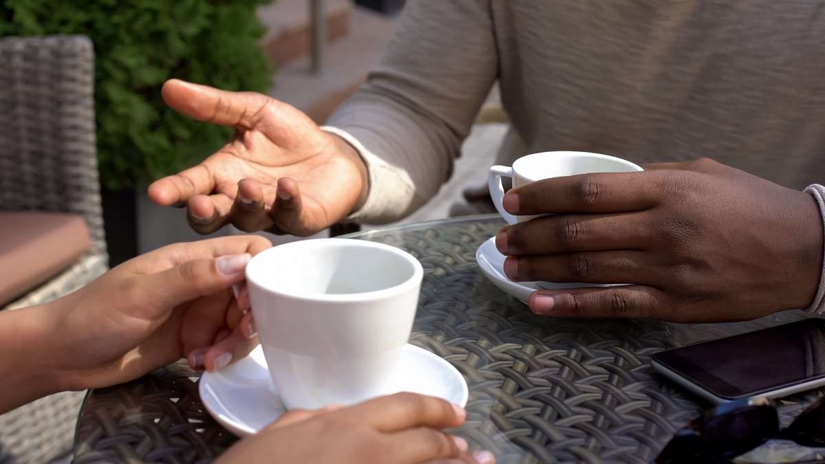 black man talking to woman sitting in cafe, colleagues drinking coffee together