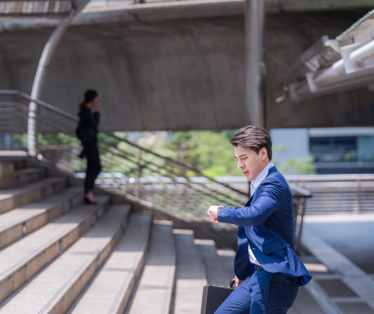 Man running late outside checking his watch.