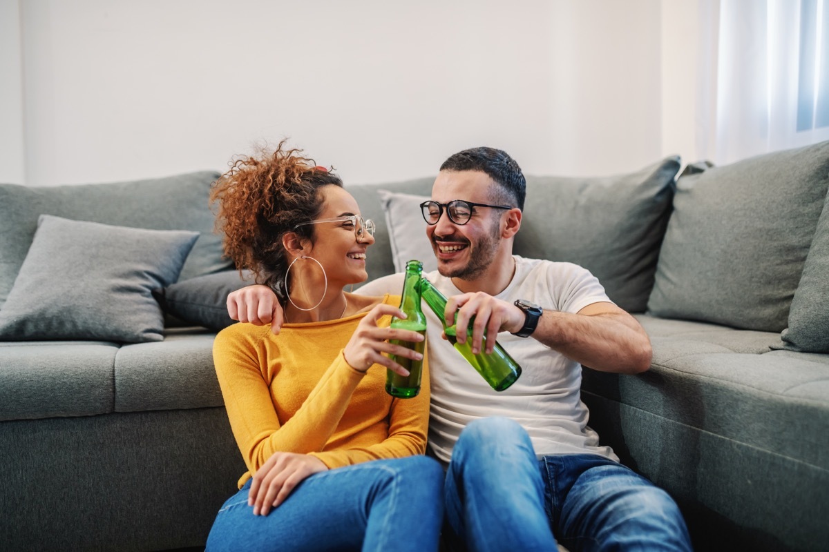 Young handsome couple relaxing at home. They are toasting with beer. Sunday afternoon.