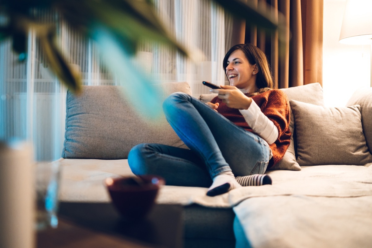 young woman watching something funny on the tv on her couch