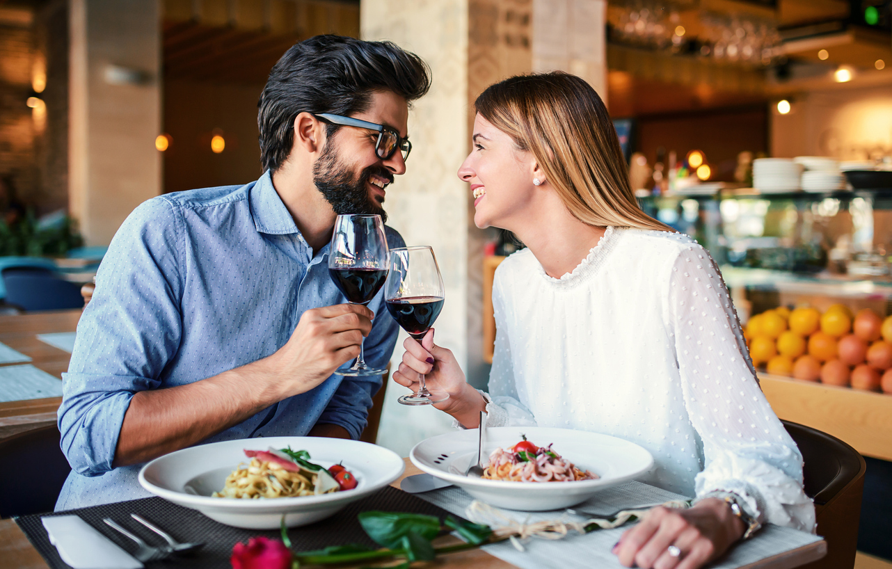 Romantic couple enjoying lunch in a restaurant, eating pasta and drinking red wine. 