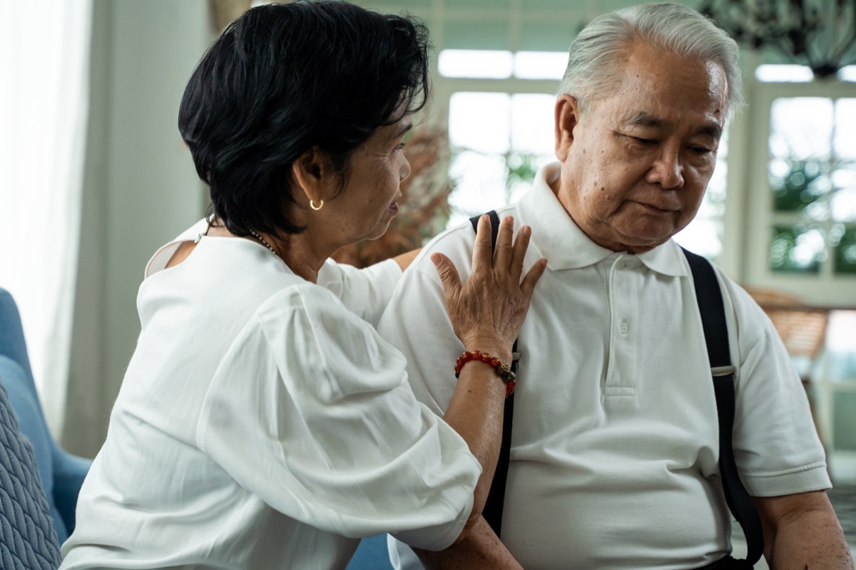 senior couple sitting on the sofa while elderly wife comforting her sad husband at home