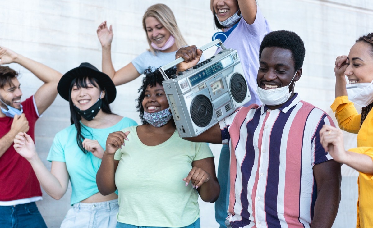 Happy people from different races dancing outdoor while listening music from old boombox stereo