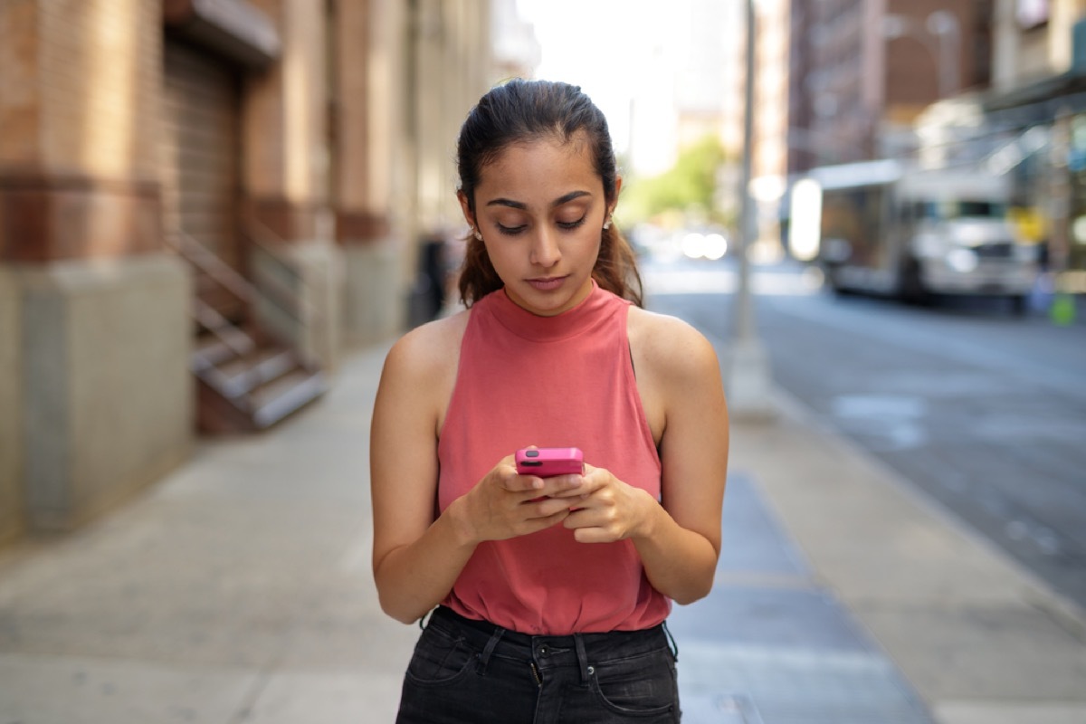 woman texting and walking on urban street