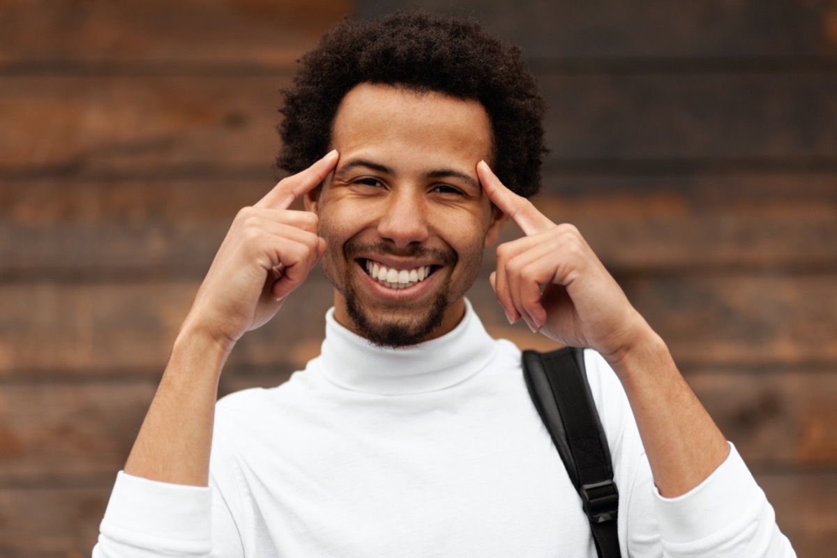 Smiling African man holds his hands at his head.