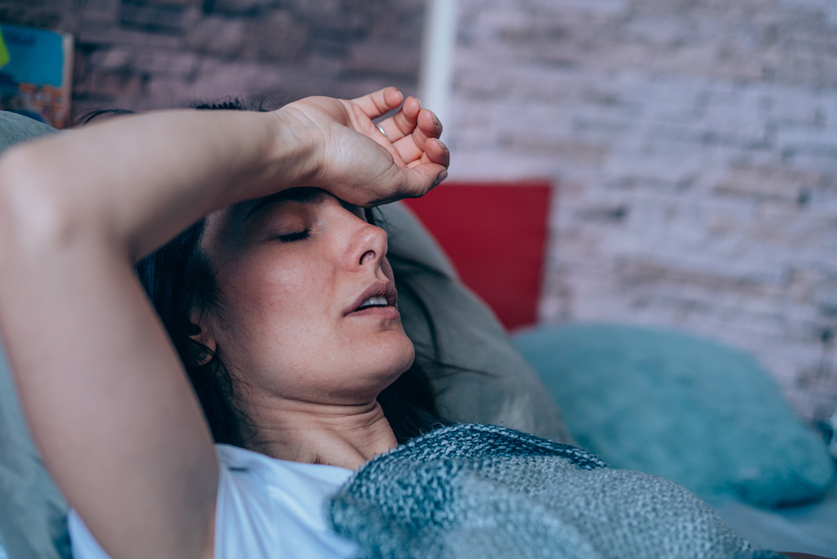 Sick woman lying in the bed covered with blanket with high temperature.