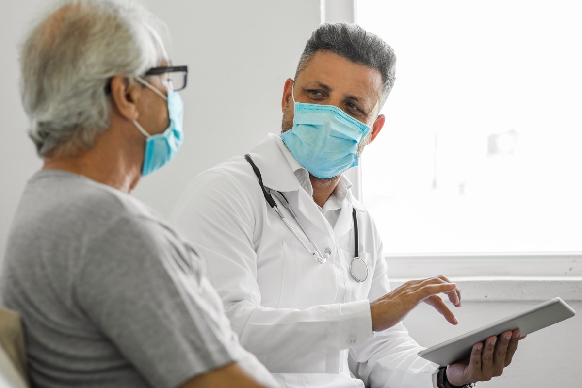 Doctor using digital tablet and talking to patient at home