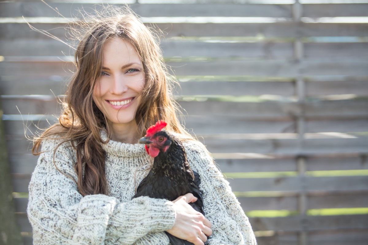 Happy young woman holding his chicken in the backyard