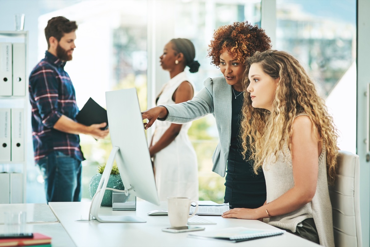 black woman showing her white woman coworker something on the computer at the office