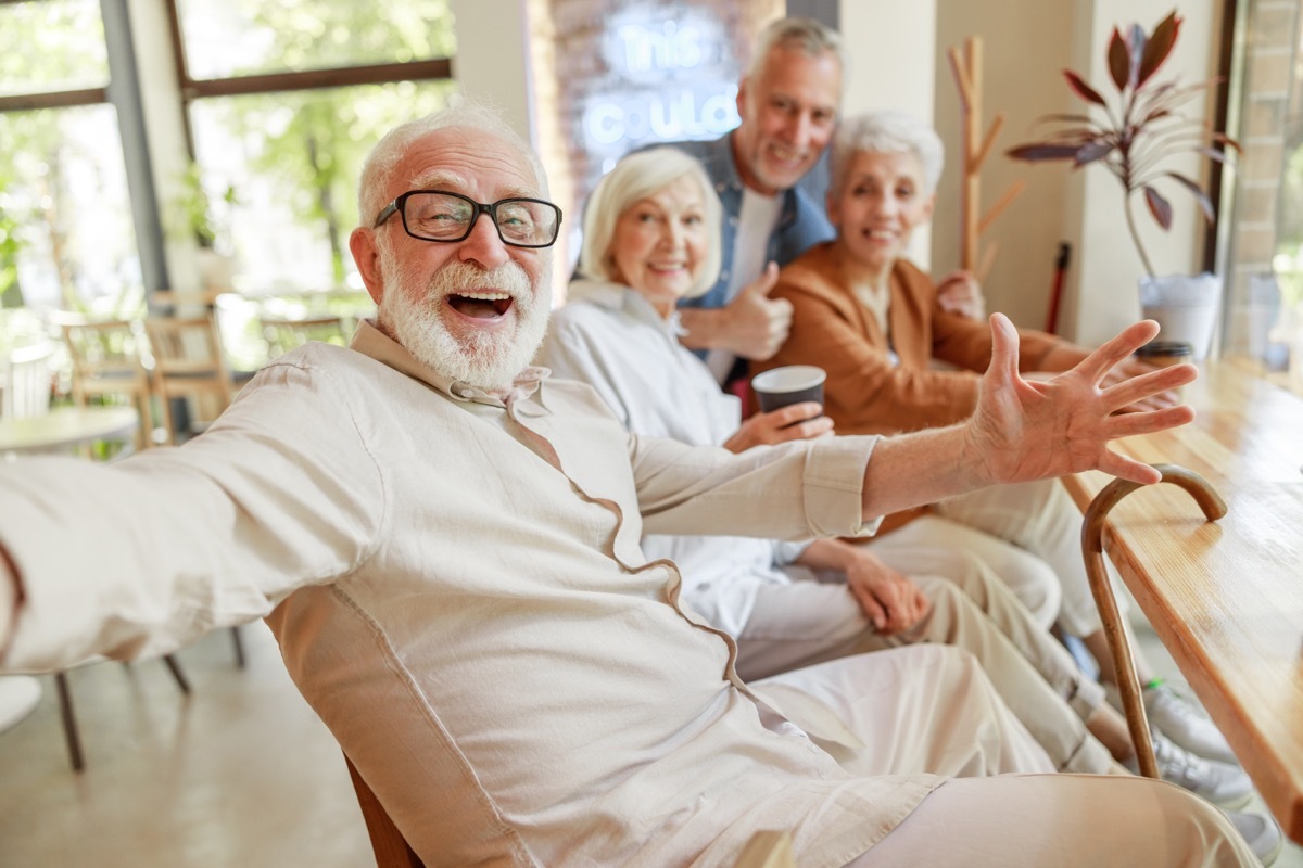 Joyful senior man spending time with friends at coffee shop