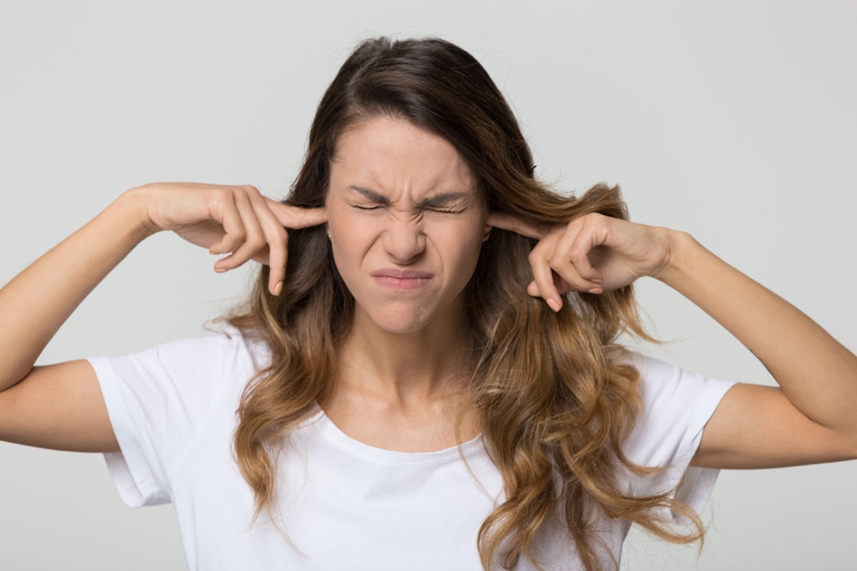 woman in a white shirt plugging her fingers in her ears