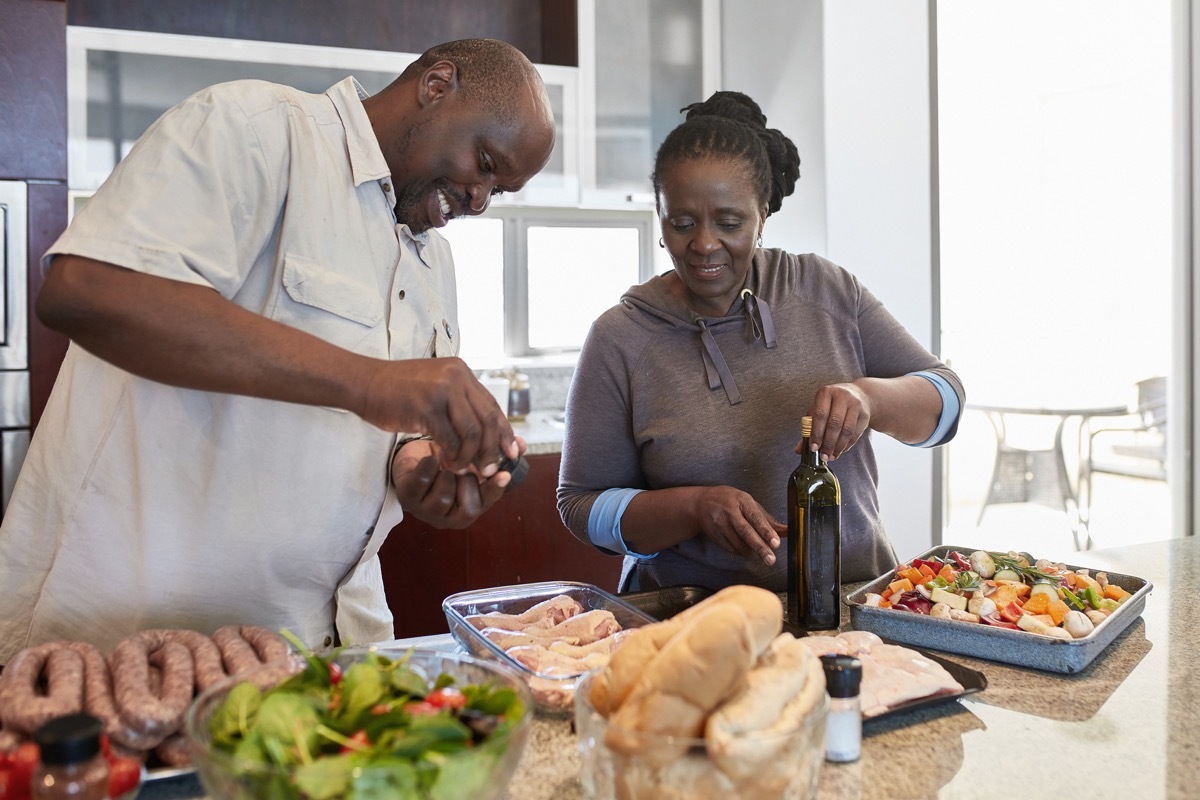 Senior couple preparing food at kitchen counter. Female is looking at male seasoning meat. They are at home. (Senior couple preparing food at kitchen counter. Female is looking at male seasoning meat. They are at home.