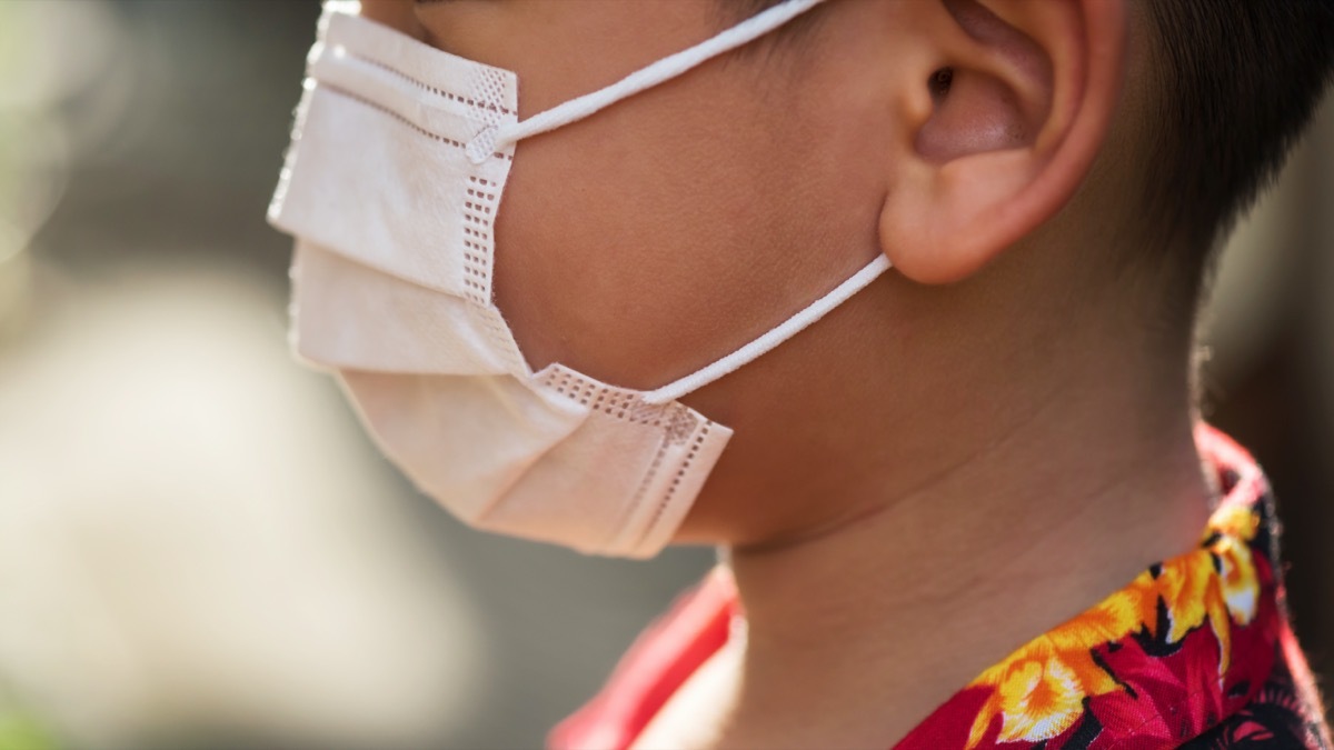 Asian boy with red hawaii shirt wearing white medical mask to prevent covid-19 or coronavirus pandemic disease with copy space for text