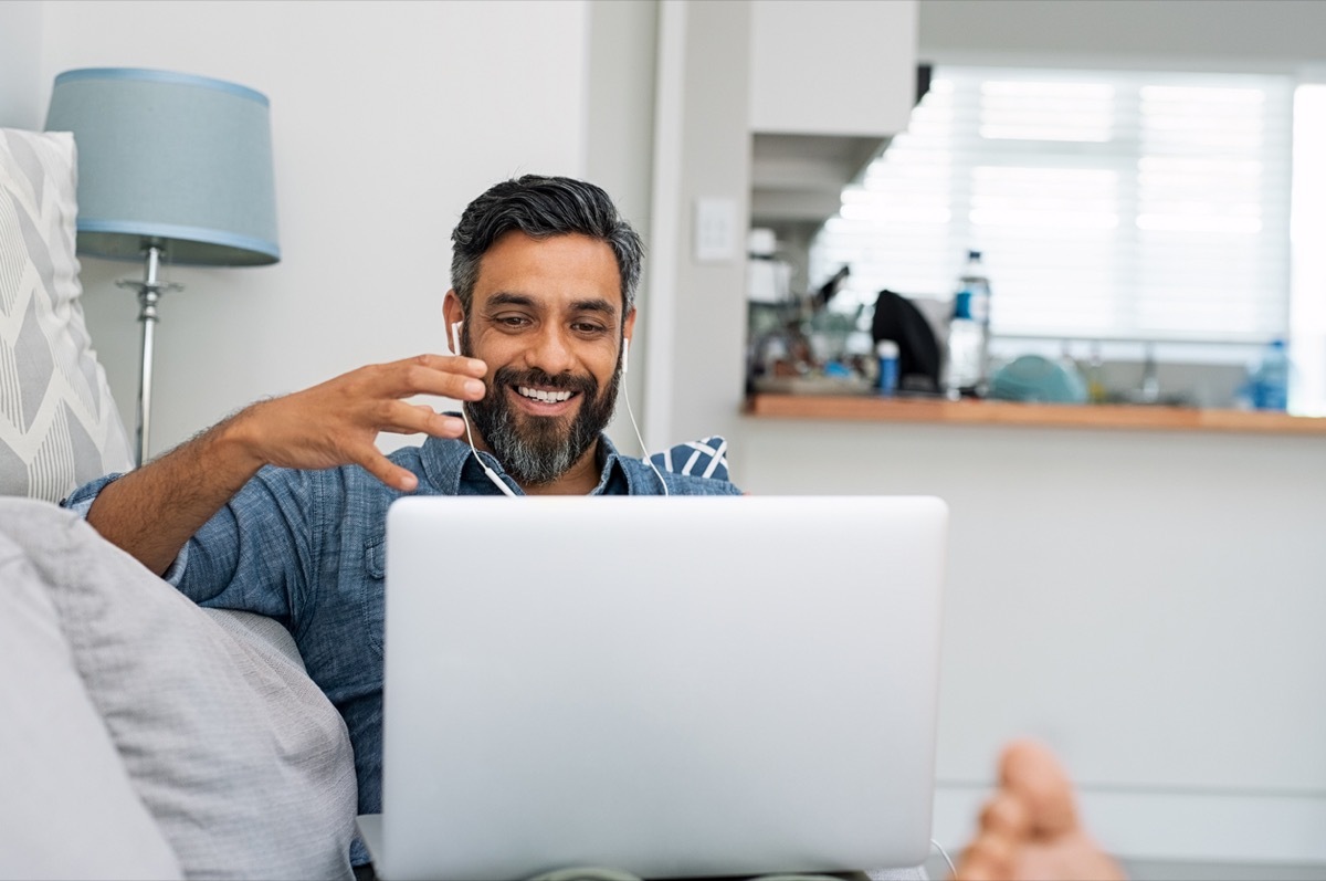 middle-aged man of color relaxing on couch while video calling using laptop at home