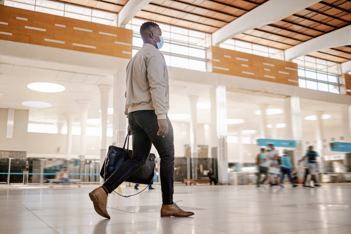 businessman travelling alone and walking in a train station while wearing a mask for protection against coronavirus