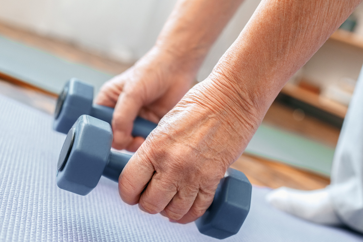 Senior man exercising indoors holding dumbbells down near the floor 