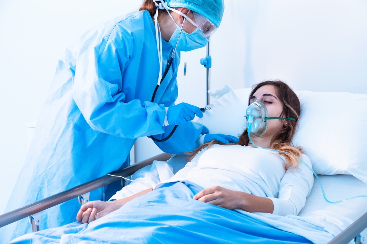 Doctor examining female patient in critical health conditions using a stethoscope in the intensive care unit of a modern hospital during covid-19 pandemic