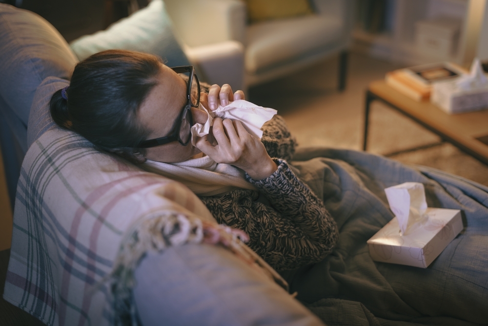 A young woman blowing her nose while sick on the couch with COVID or the flu