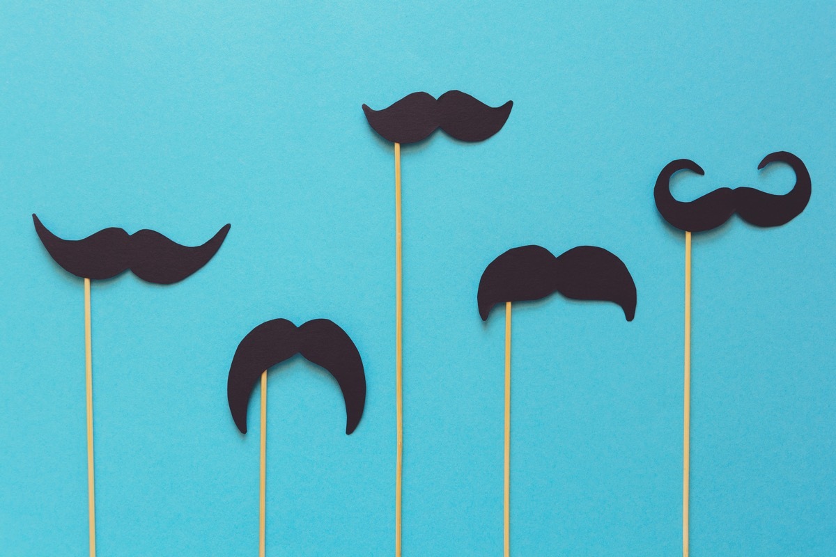 Paper moustache on booth props on blue paper background. Cut out style. Movember concept. Top view. Flat lay. Copy space. Toned (Paper moustache on booth props on blue paper background. Cut out style. Movember concept. Top view. Flat lay. Copy space.