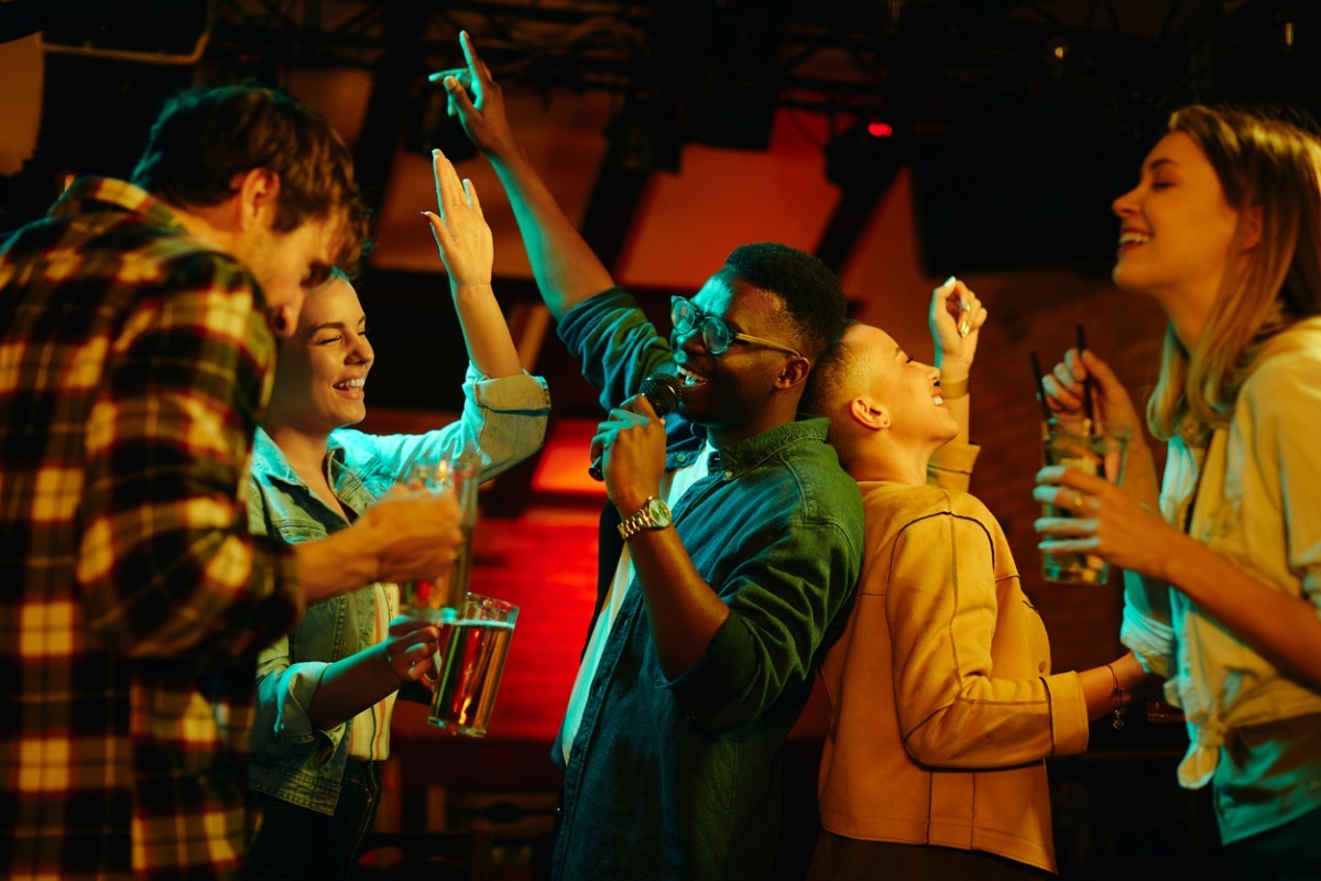 man singing karaoke in group of friends