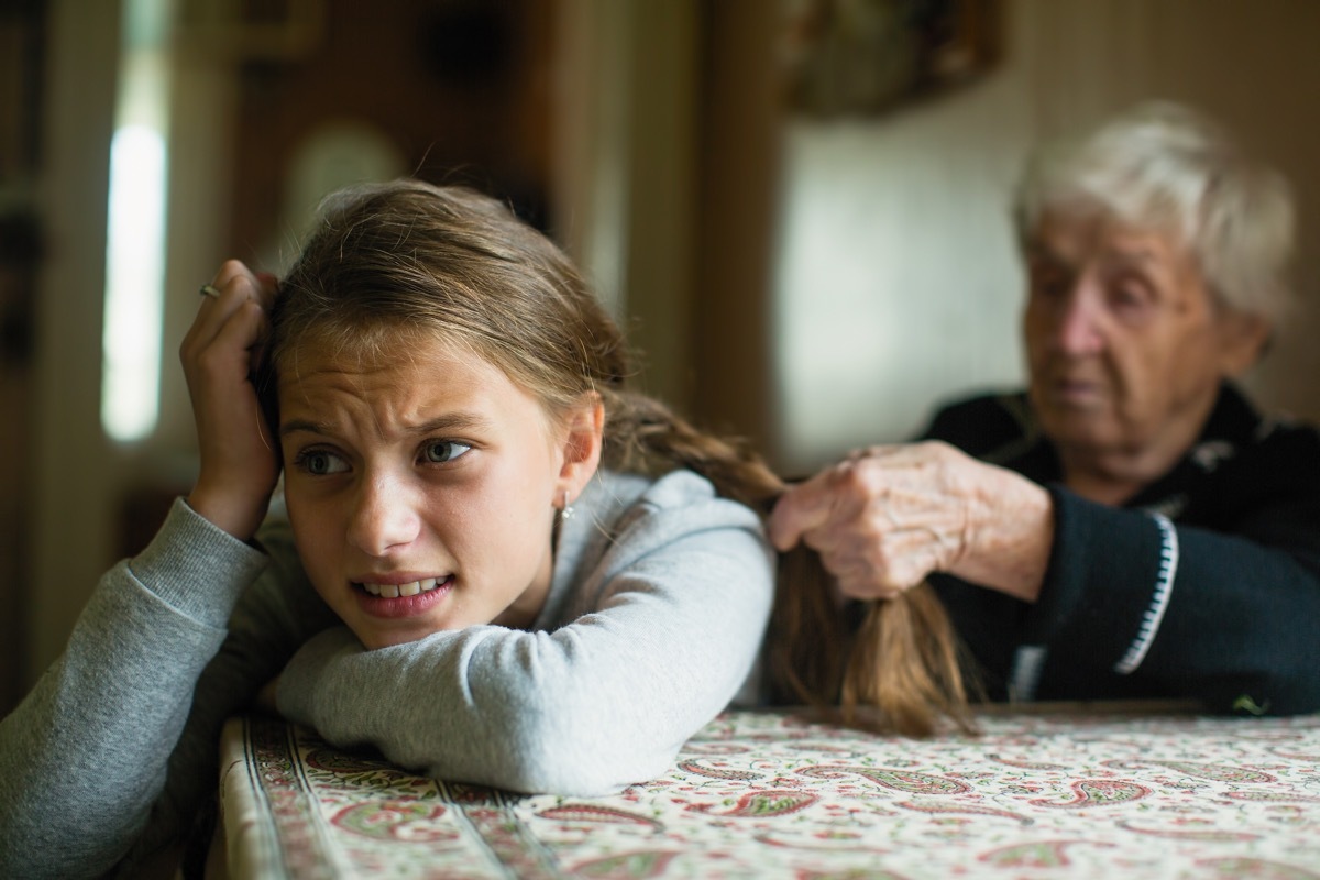 upset girl having hair braided by her grandmother