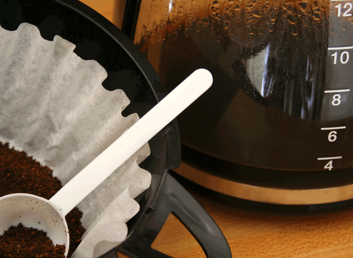 ground coffee in filter with spoon next to coffee pot