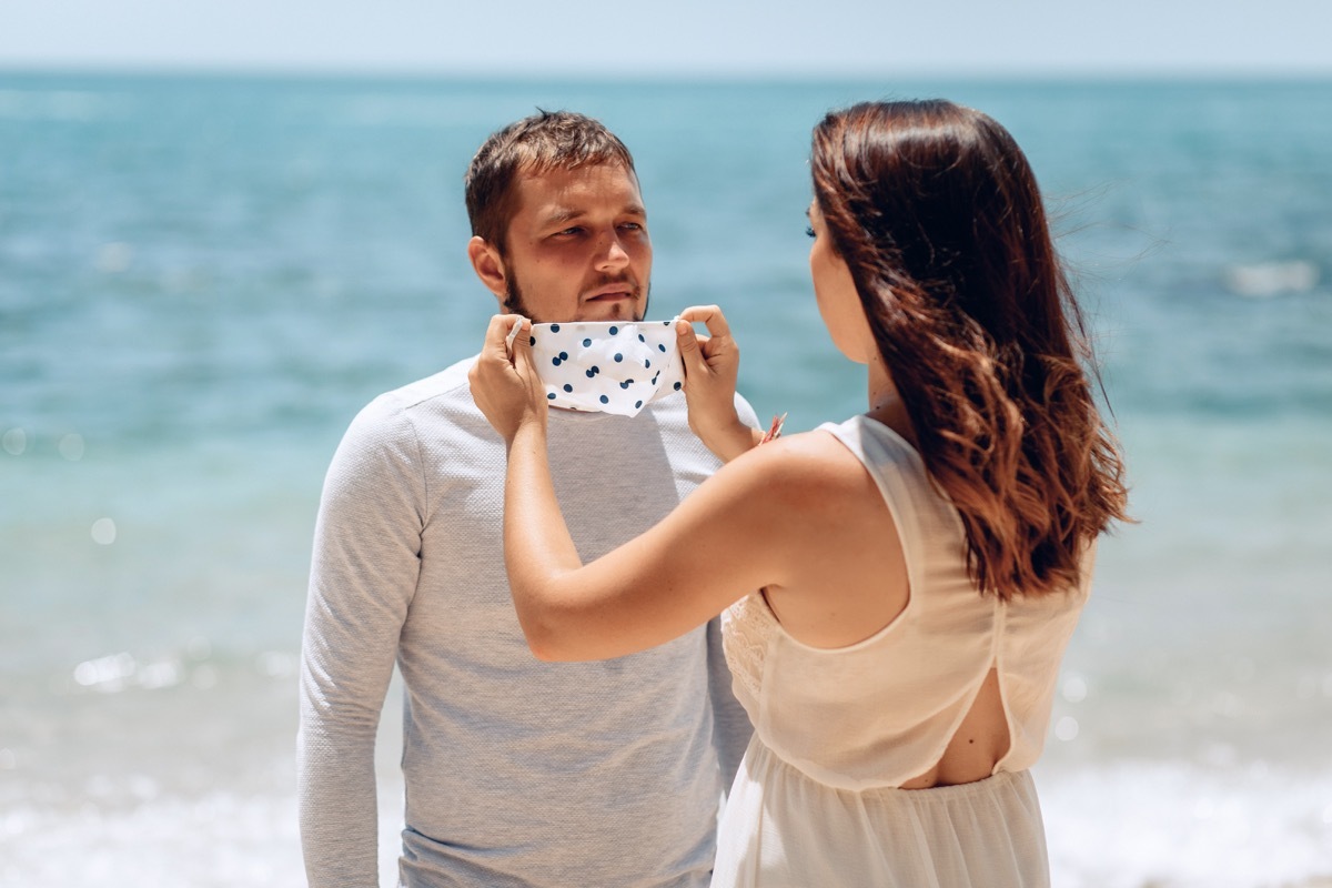 woman putting mask on man outdoors