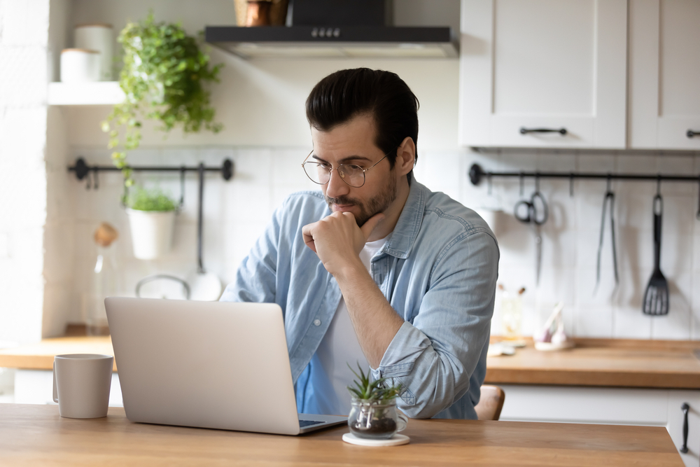 A young man sitting in his kitchen using a laptop to check his email