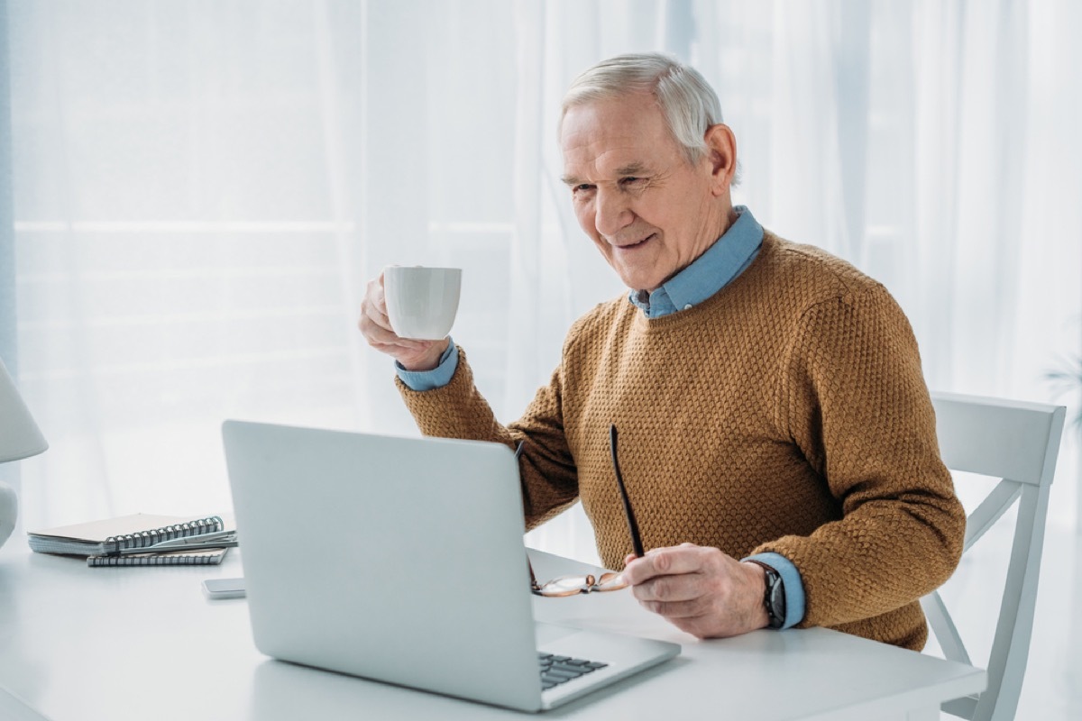 older white man sipping coffee while on his laptop