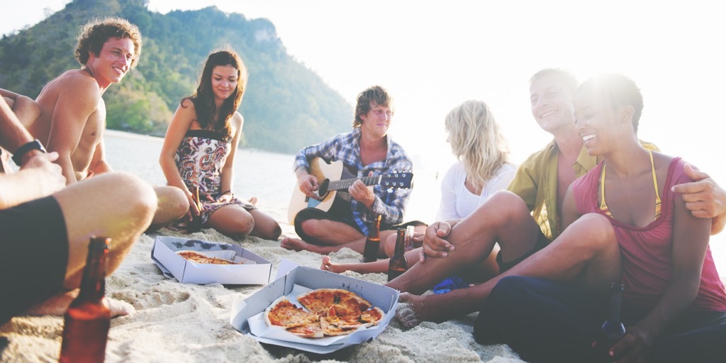 group of friends sitting in a circle on the beach and eating pizza