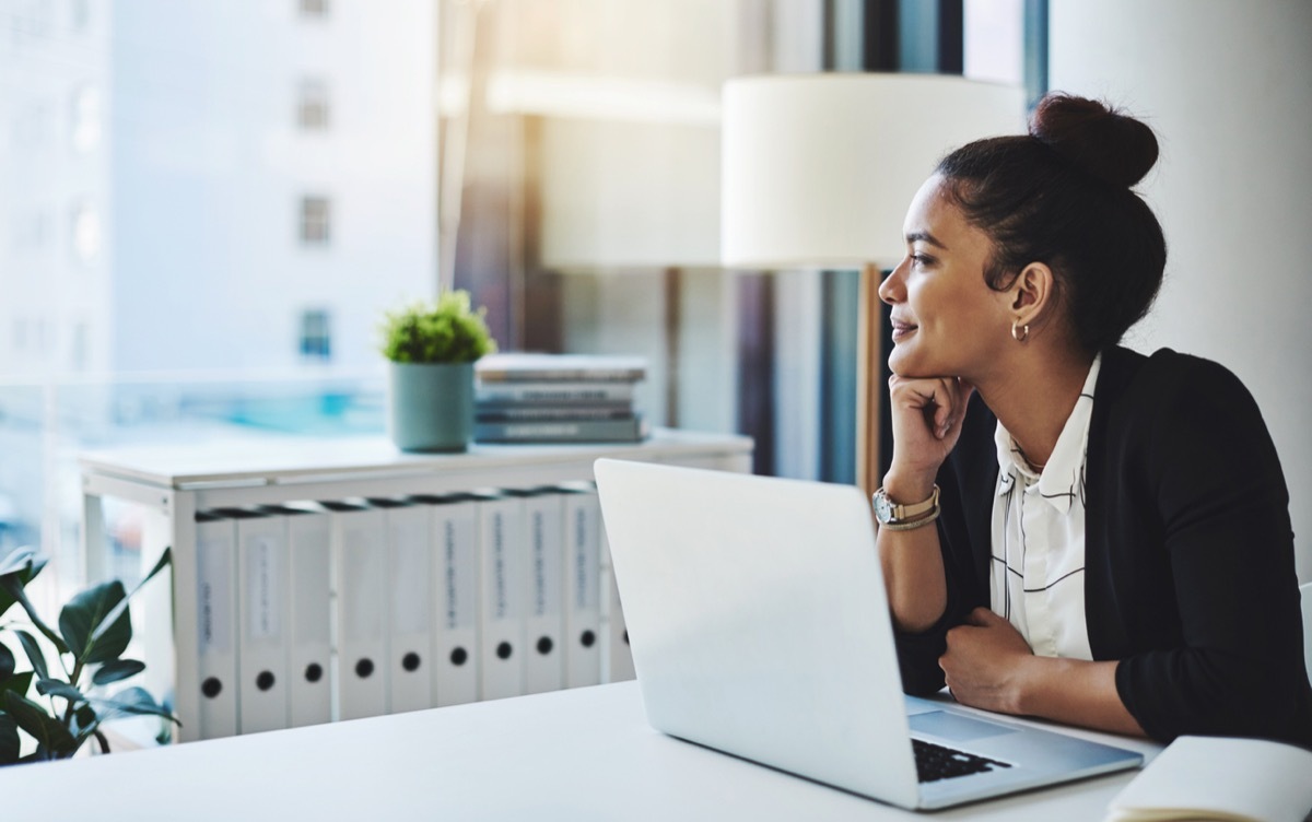 latina woman at laptop in office looking out the window